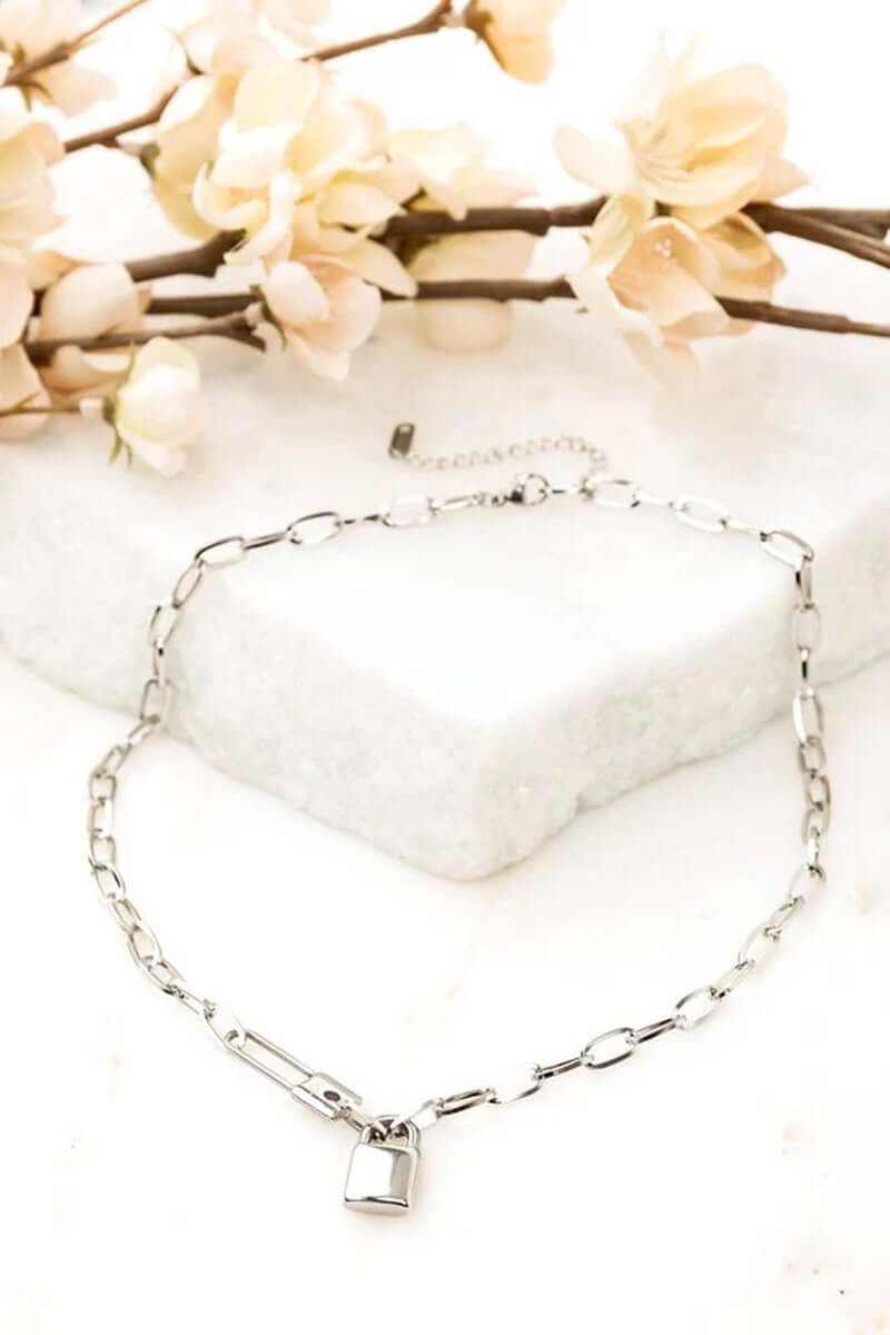 18K stainless steel lock and clip chain necklace on a marble surface with floral accents.