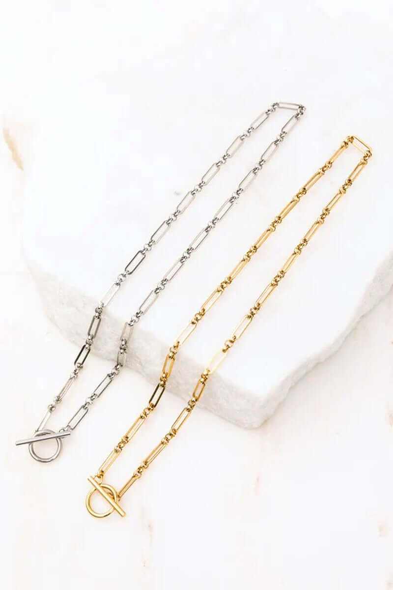 18K stainless steel toggle chain necklaces in gold and silver on a marble surface, showcasing waterproof and tarnish-resistant features.