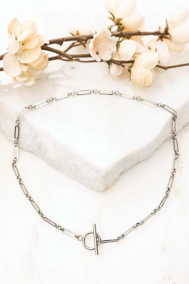 18K stainless steel toggle chain necklace on marble surface with flowers, tarnish resistant and waterproof design.