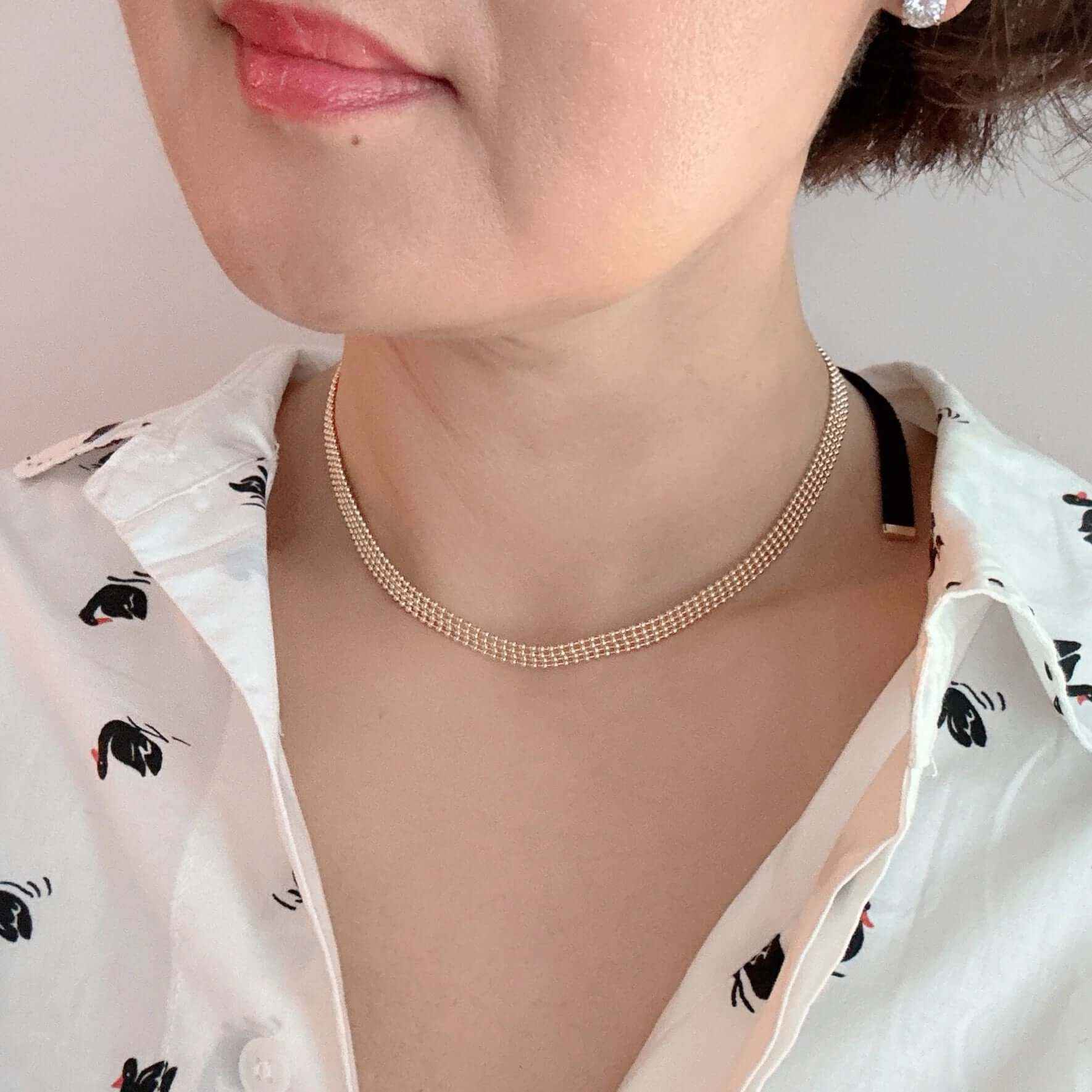 Close-up of a woman wearing an adjustable gold tie back choker necklace with layered gold beads, styled with a printed shirt.