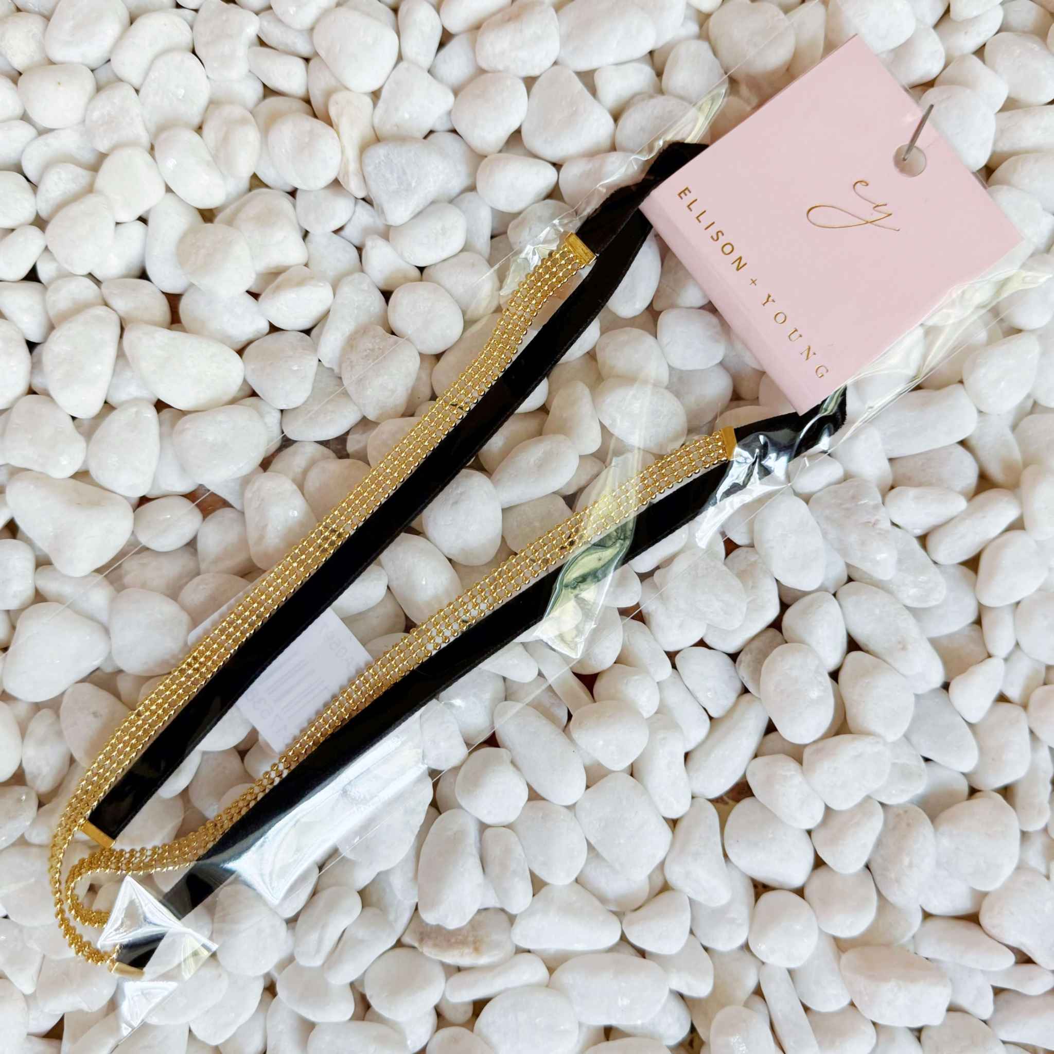 Adjustable gold tie back choker necklace with velvet sash ties and layered gold beads on white pebbles.