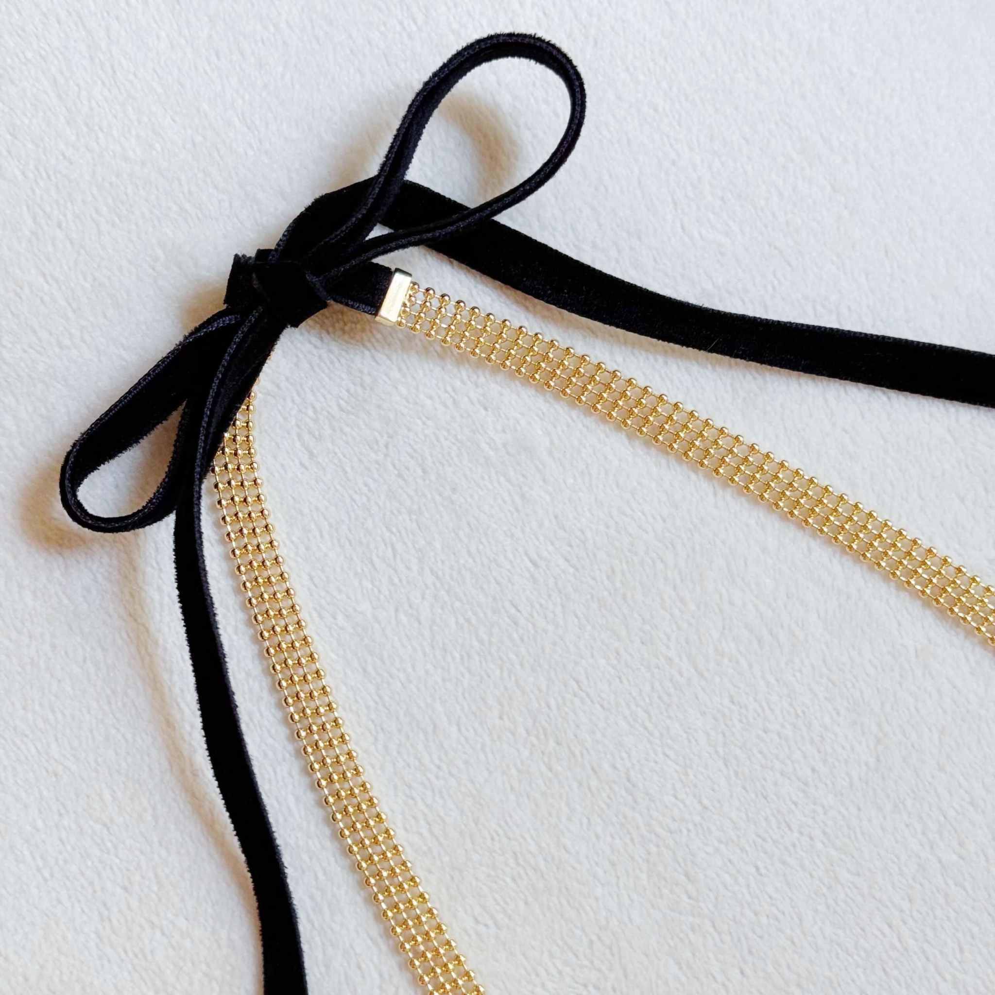 Adjustable gold tie back choker necklace with black velvet sash and layered gold beads on a light background.