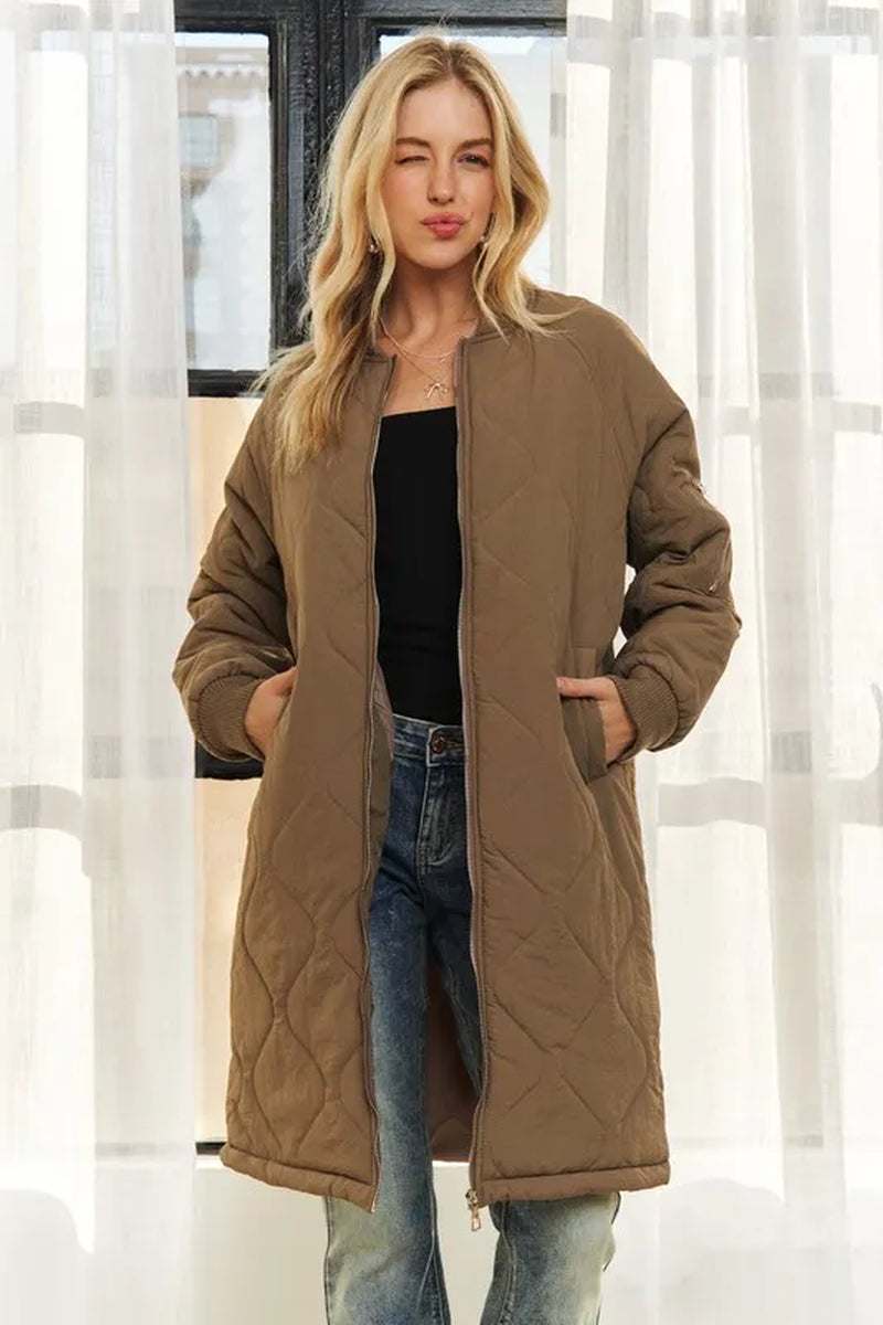 woman wearing brown ADORA zip up long utility jacket with pockets and quilted design standing indoors