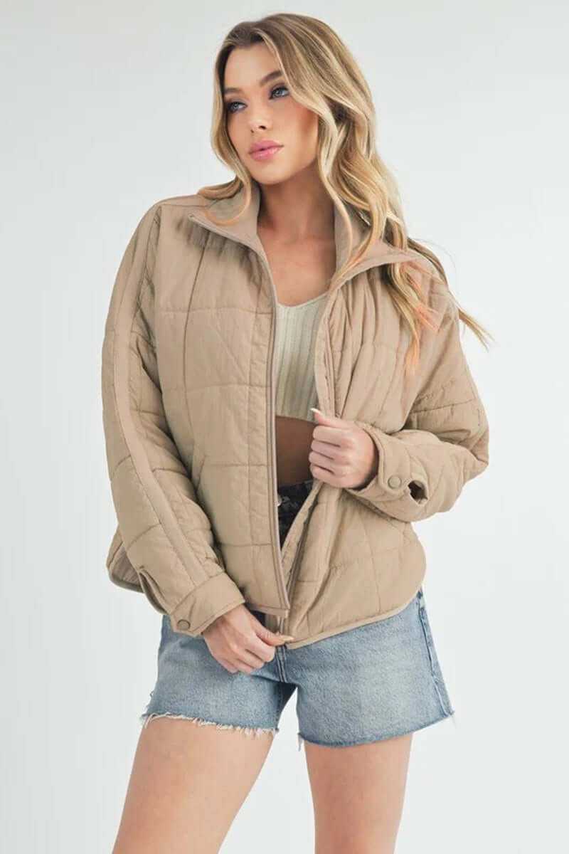 Woman wearing a Bebe puffer jacket, styled with shorts, showcasing its oversized silhouette and front zip closure.
