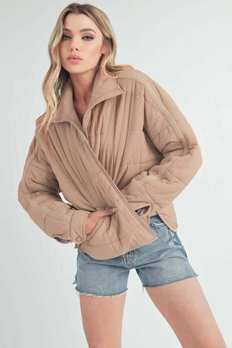 Woman wearing a stylish tan Bebe puffer jacket paired with denim shorts for a casual look.