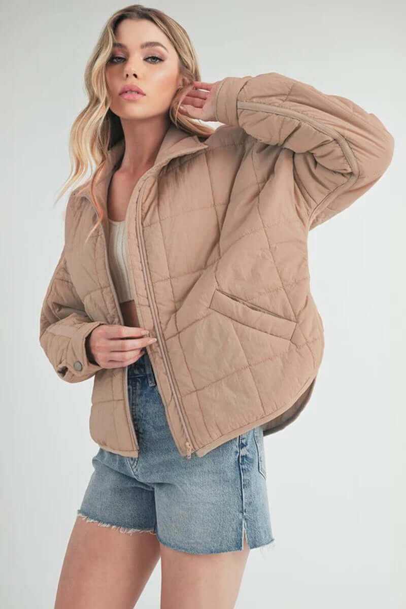 Model wearing beige Bebe puffer jacket, showcasing oversized fit and front zip closure for casual style.