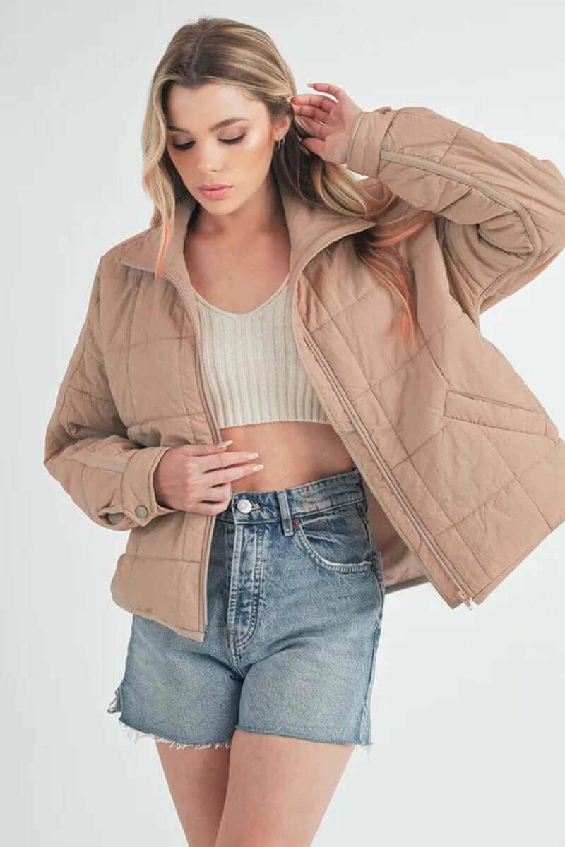 Bebe puffer jacket in beige worn with a cropped top and denim shorts, showcasing a stylish, oversized look.