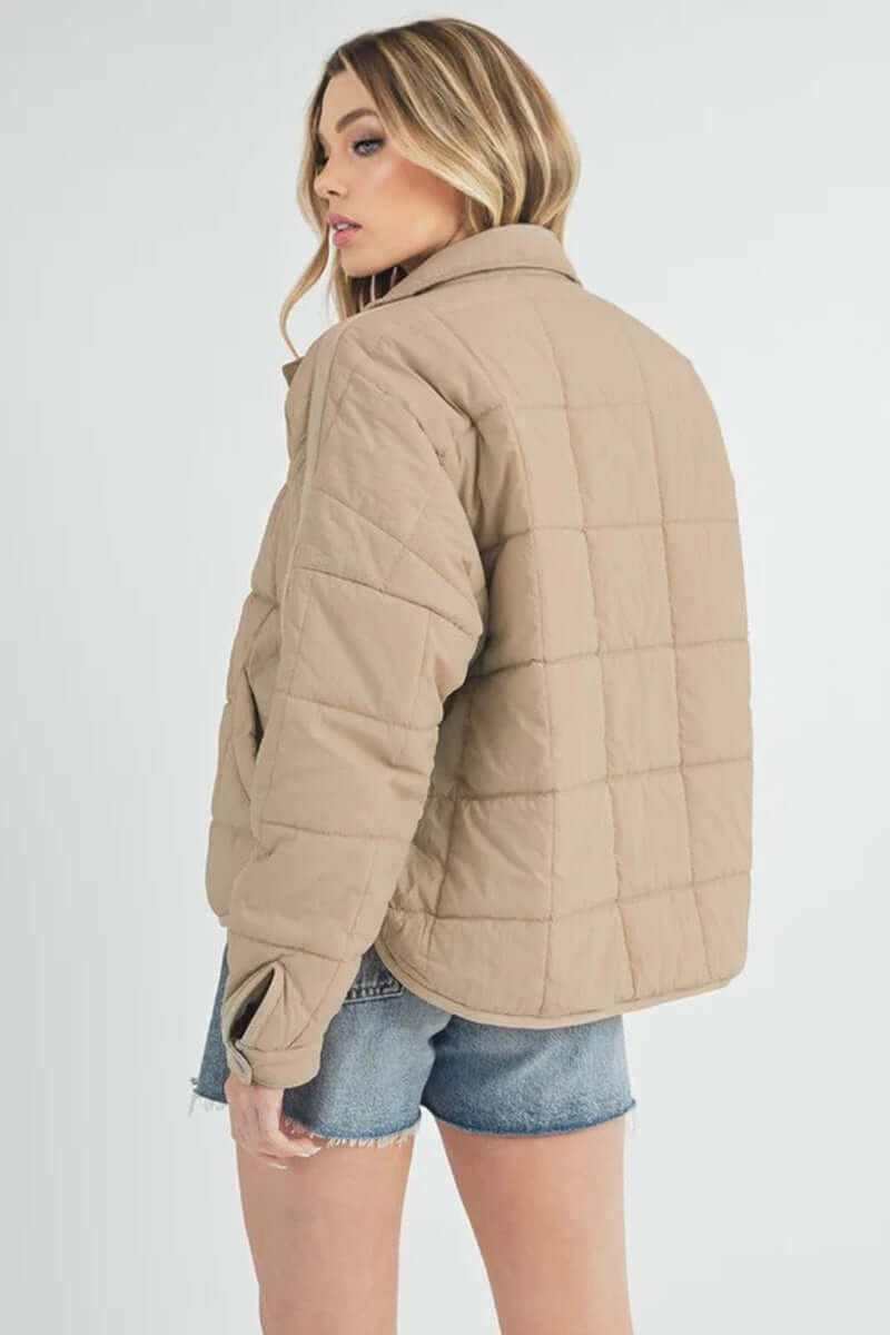 Stylish woman wearing a beige Bebe puffer jacket, showcasing its oversized boxy silhouette and quilted design.