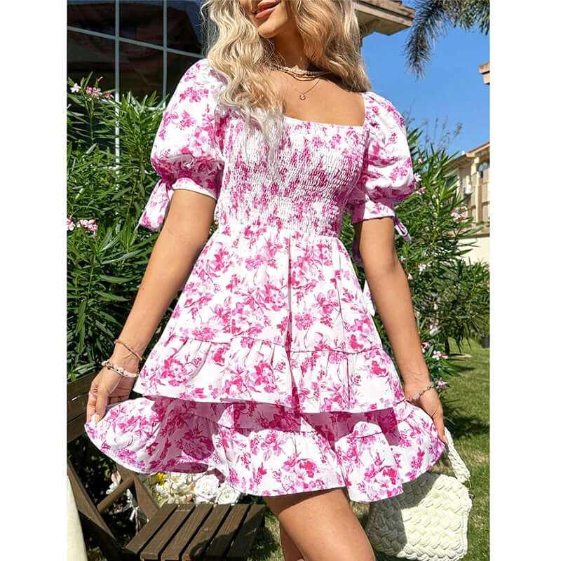 Women's pink floral puff sleeve mini dress with square neck, smocked bodice, and ruffle hem in sunny outdoor setting.