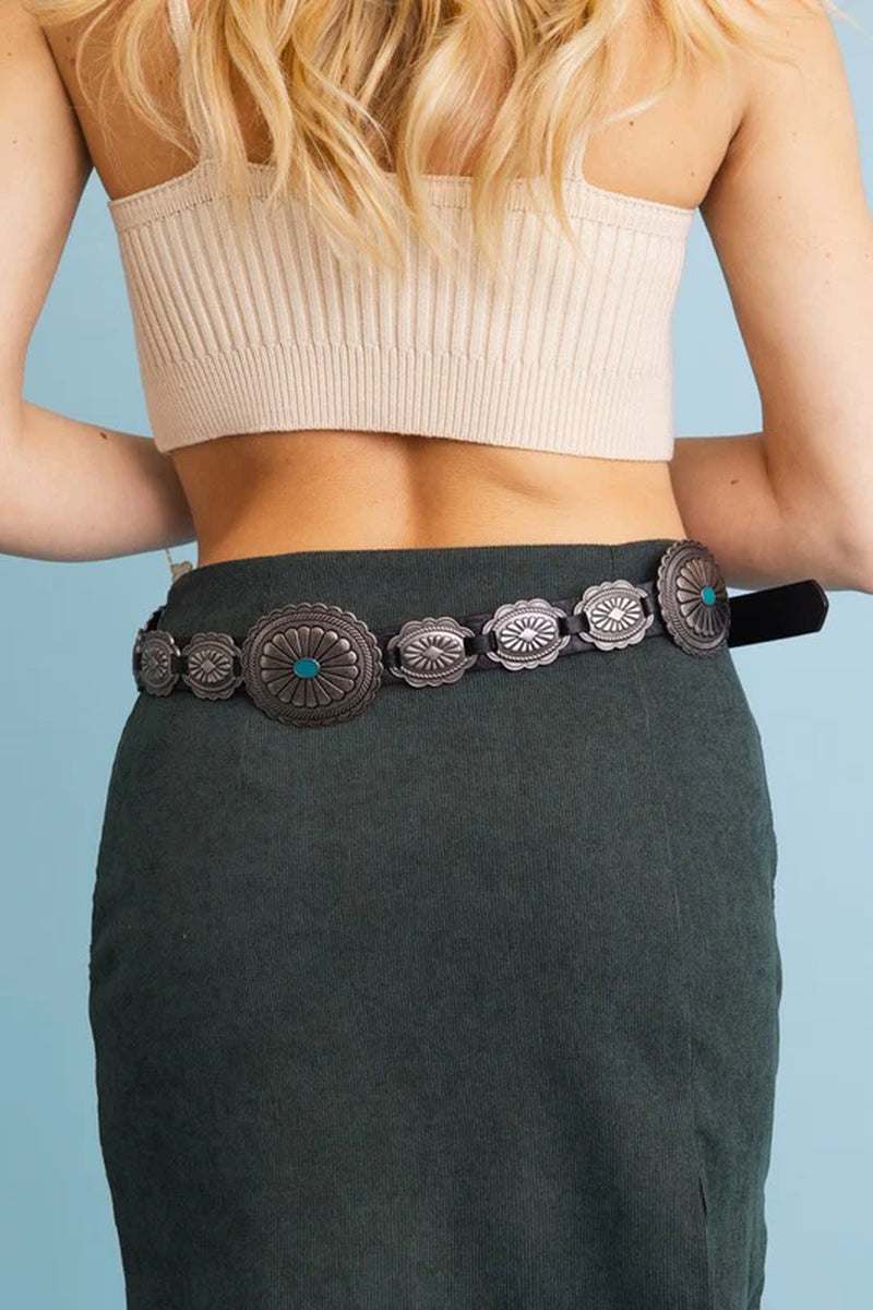 Woman wearing a Boho Turquoise Western Concho Belt over a green skirt, showcasing intricate silver conchos with turquoise accents.