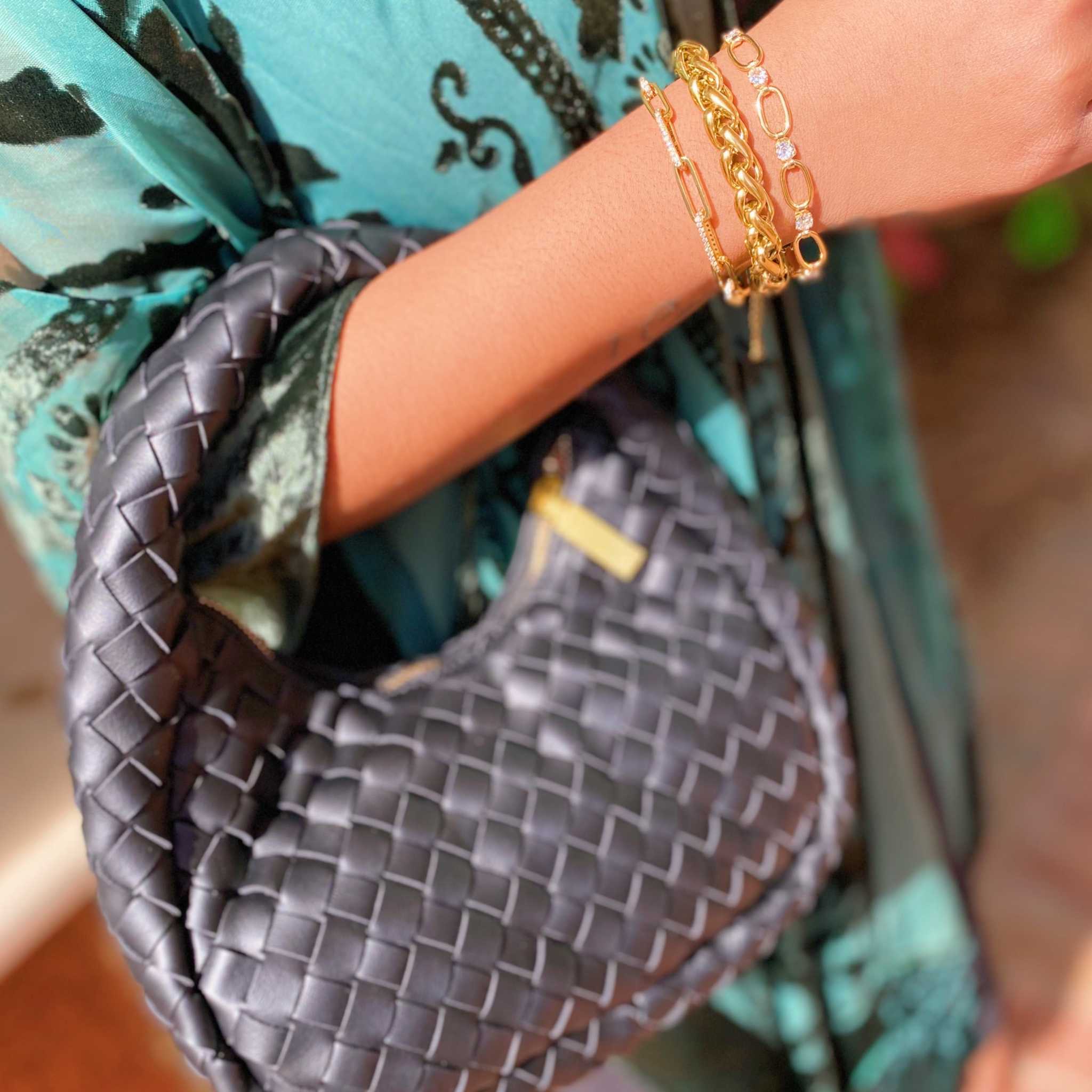 Close-up of a hand wearing a bold and edgy fashion chain bracelet while holding a braided handbag.