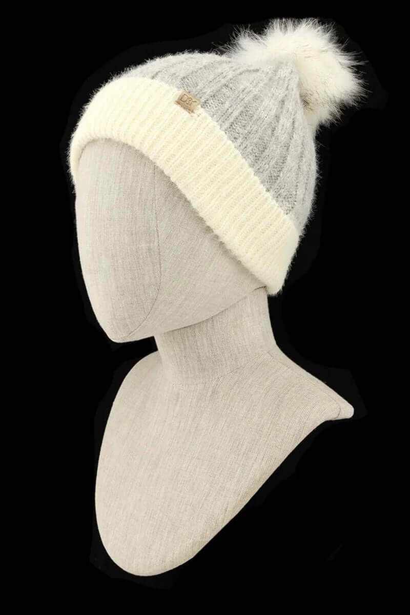 Chunky knit faux fur pom beanie in gray and white on a mannequin against a black background.