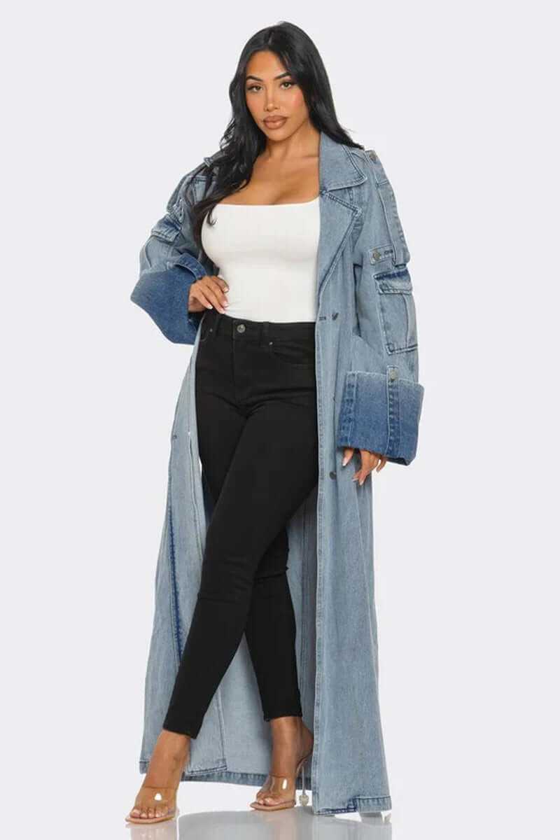 Woman wearing light wash longline denim trench coat with belted waist and oversized cuffs