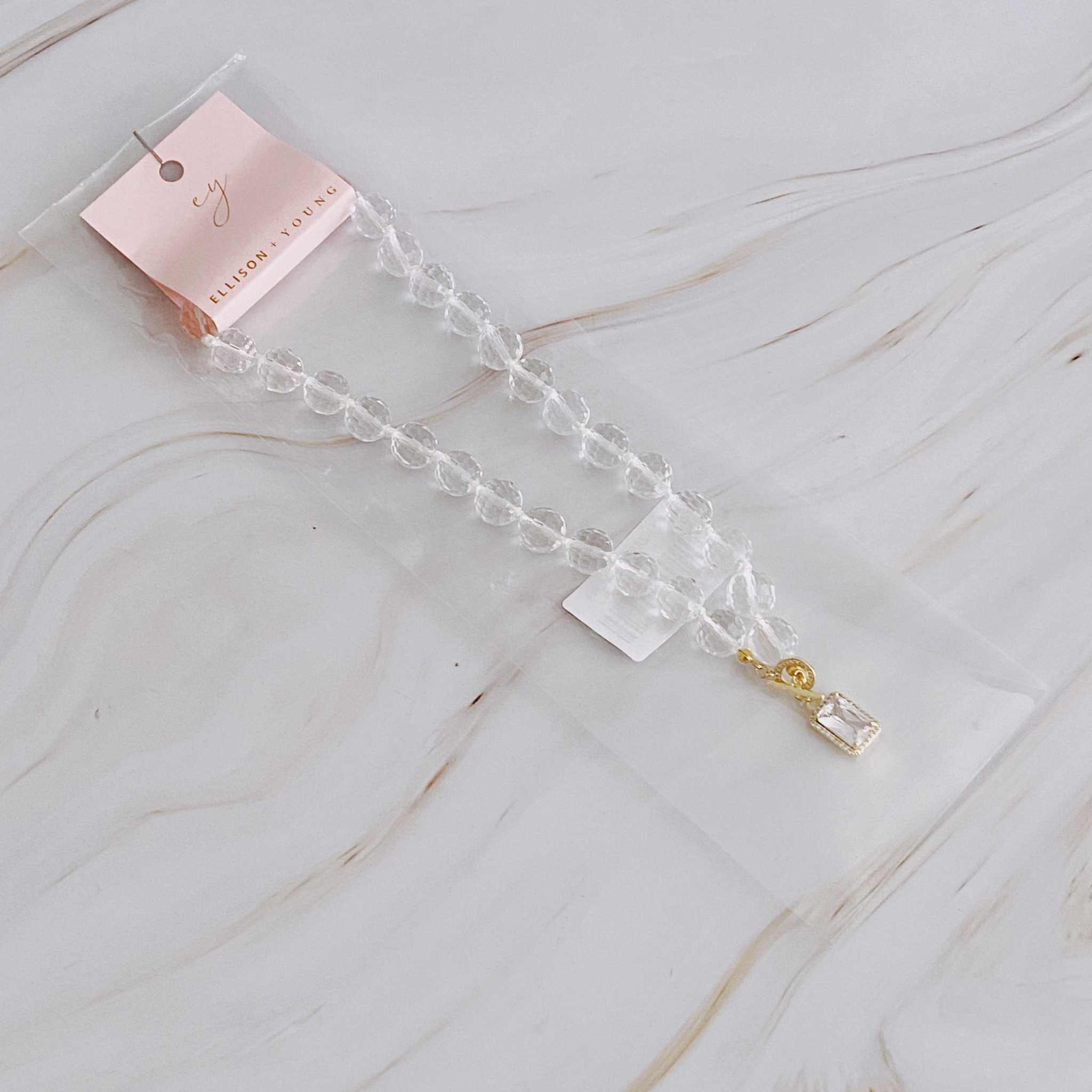 Clear crystal ball chain necklace with glass beads and gold pendant, elegantly packaged on a card.