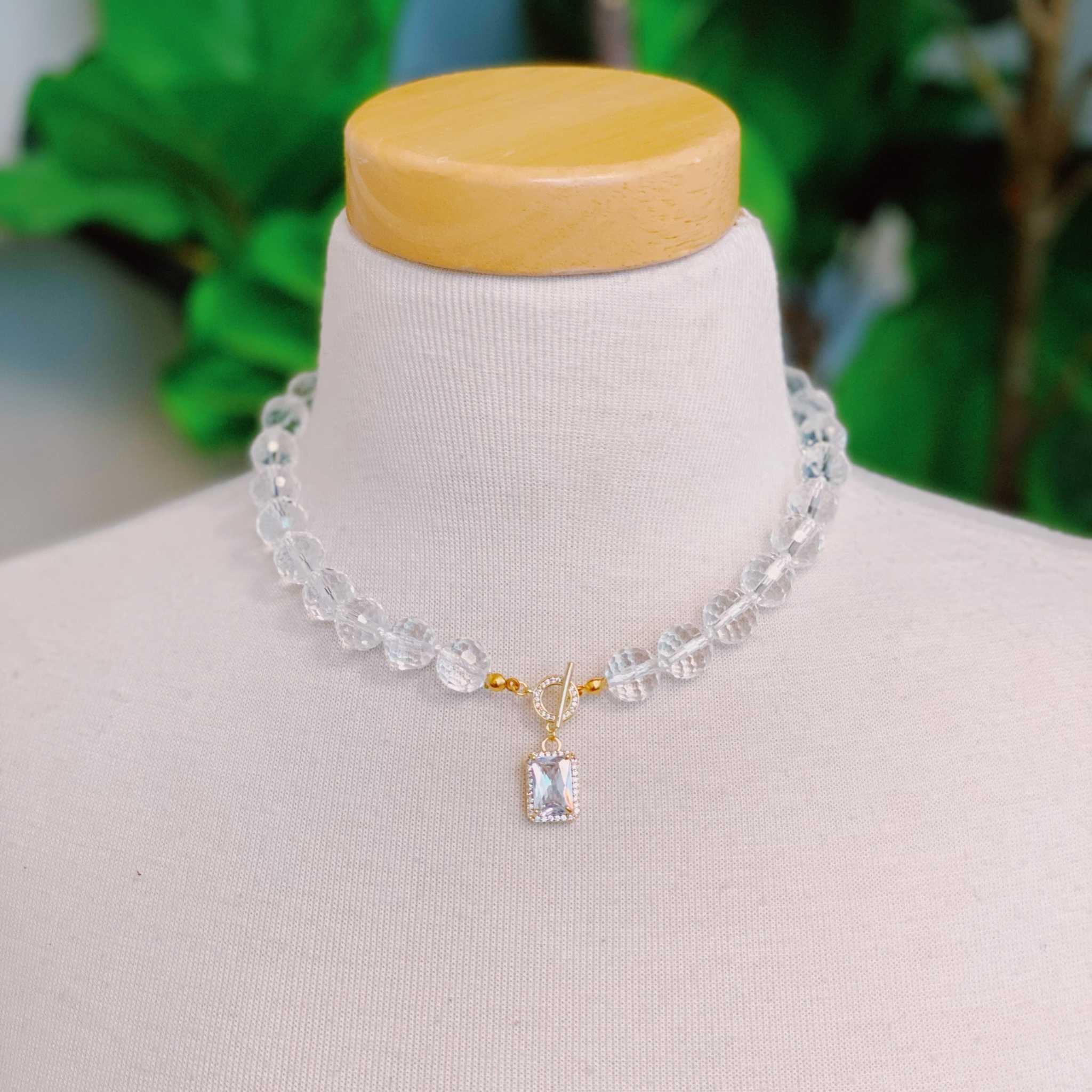 Elegant clear crystal ball chain necklace with glass beads and jeweled pendant on display.