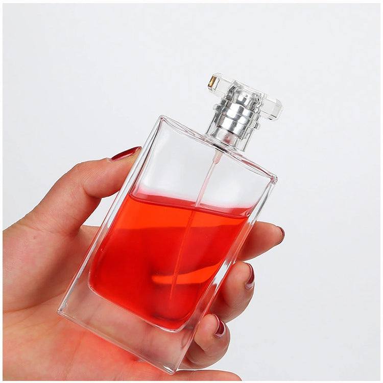Clear glass perfume bottle with silver spray cap filled with red liquid held in hand