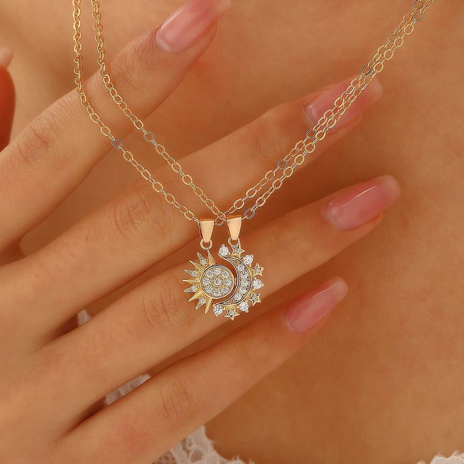 Gold couple set sun and moon necklaces with crystal accents on delicate chains worn on hand