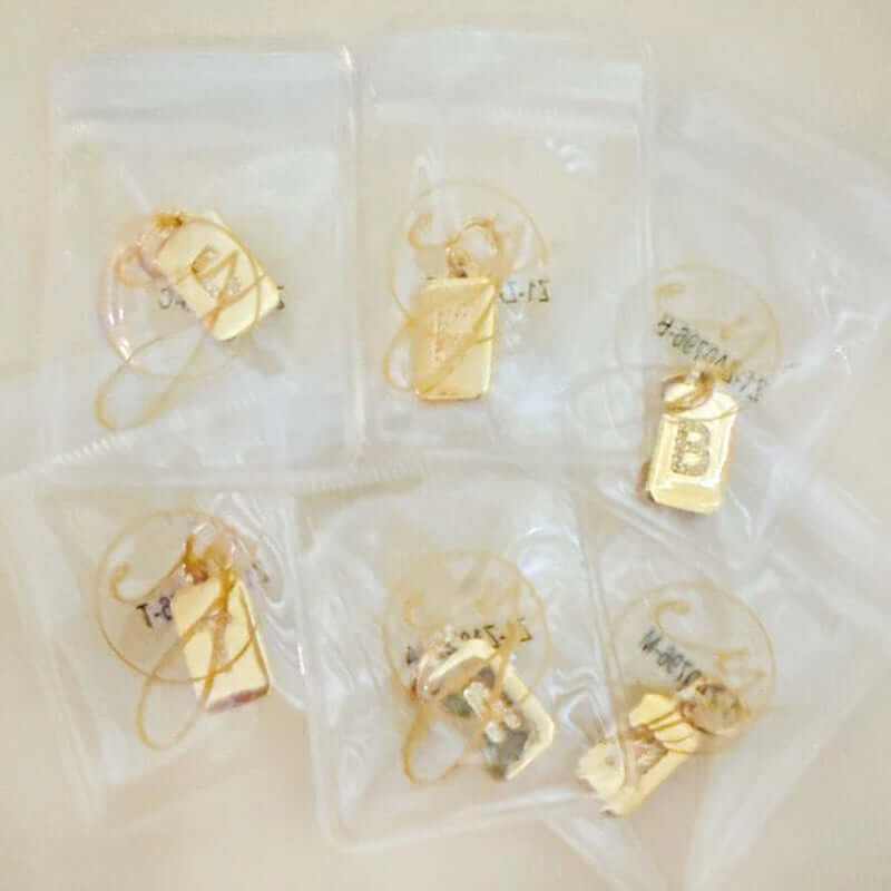 Custom personalized square initial seamless clip charms in packages, featuring gold plating and cubic zirconia.