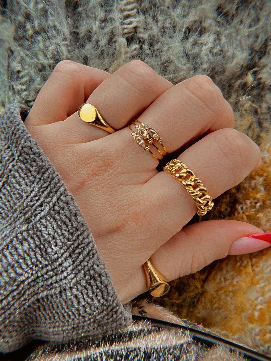 Hand wearing delicate gold-plated candy-colored pearl statement ring with other gold rings on textured fabric background