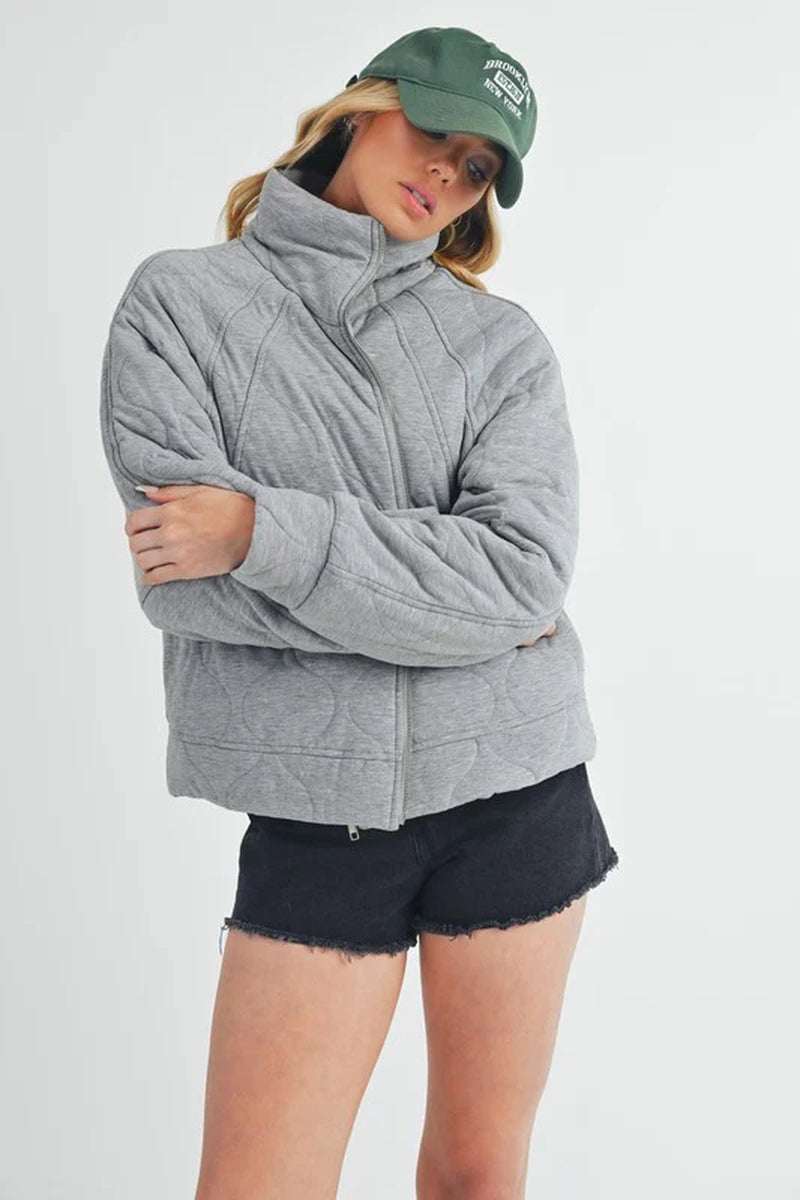 Stylish woman in a gray quilted jacket with oversized fit, shorts, and a green cap for a contemporary, cozy look.