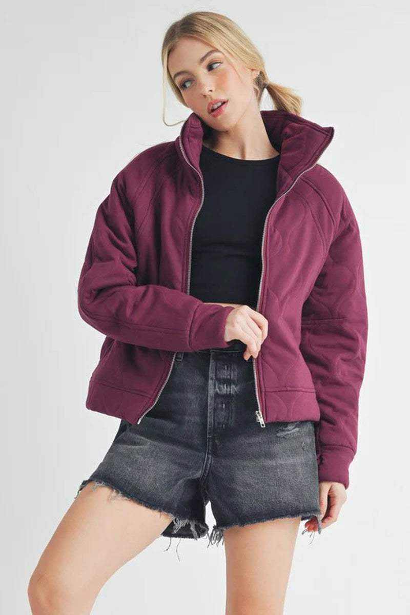 Woman wearing a cozy Darla Quilted Jacket in burgundy with a stylish black top and denim shorts.