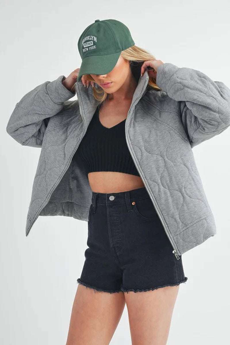 Model wearing a cozy Darla Quilted Jacket with a black crop top and shorts, complemented by a green cap.