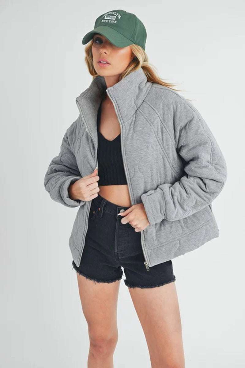 Darla Quilted Jacket in gray, featuring oversized fit and cozy design, styled with black shorts and a green cap.