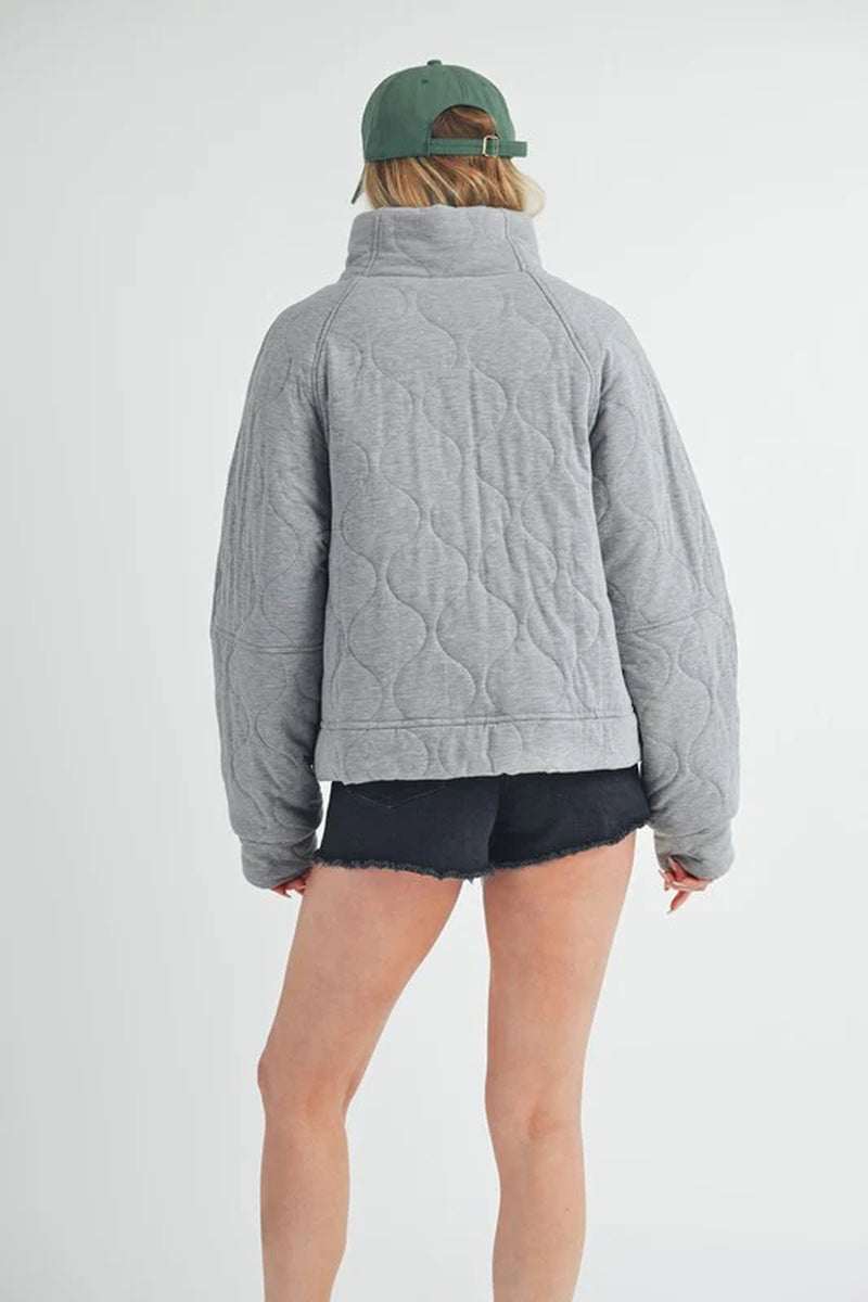 Back view of a woman wearing a cozy gray quilted jacket with oversized silhouette and relaxed fit.