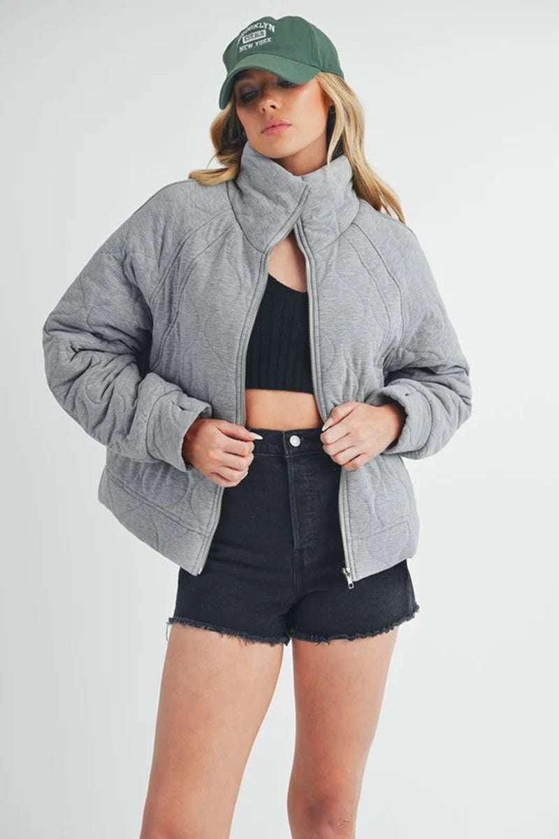 Stylish woman wearing a grey Darla quilted jacket with a relaxed fit, paired with black shorts and a green cap.