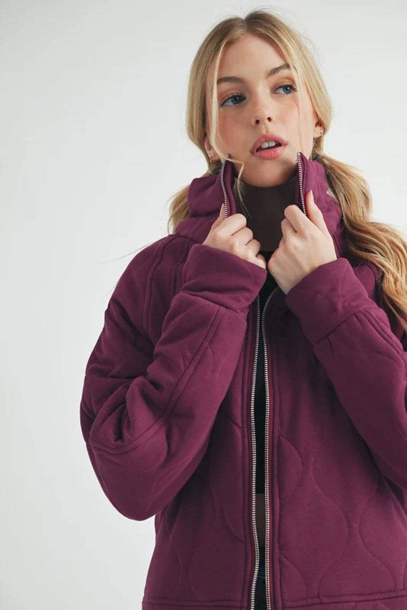 Model wearing a Darla Quilted Jacket in deep purple, showcasing its relaxed fit and stylish zipper design.