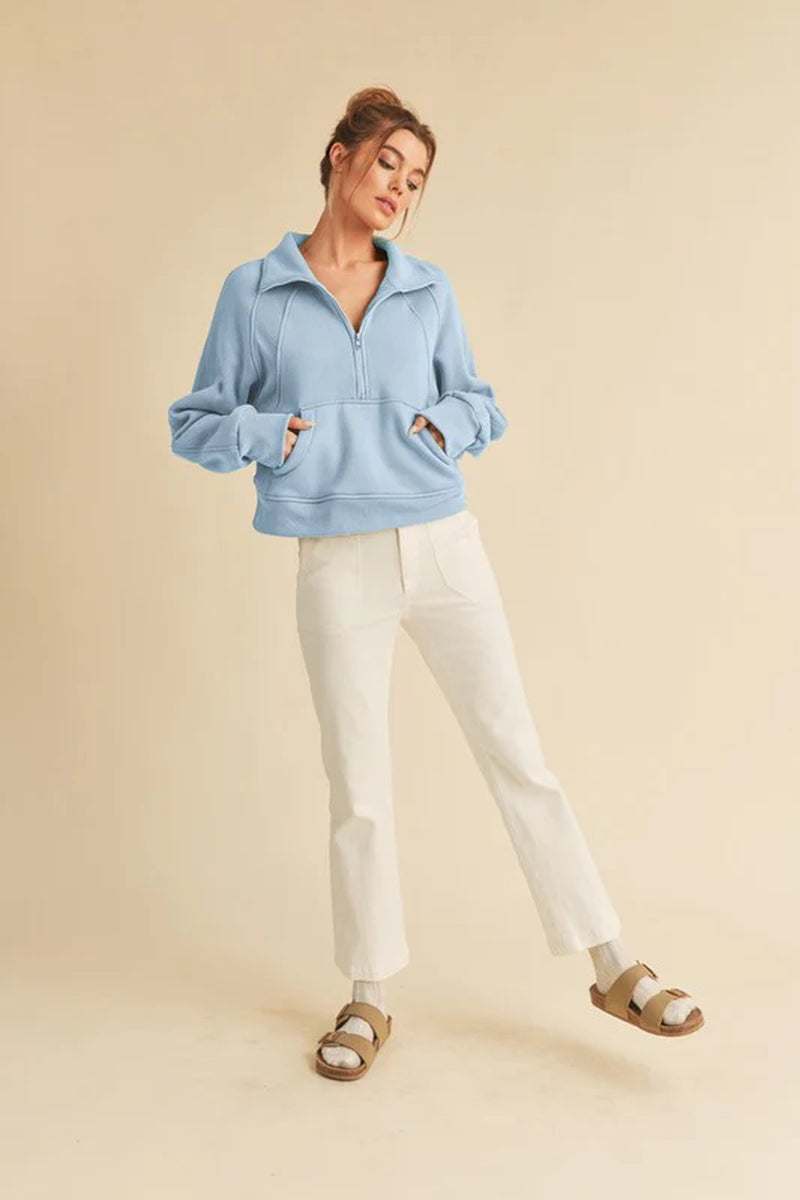 Model wearing a light blue Dove funnel neck half-zip sweater paired with white pants and sandals.