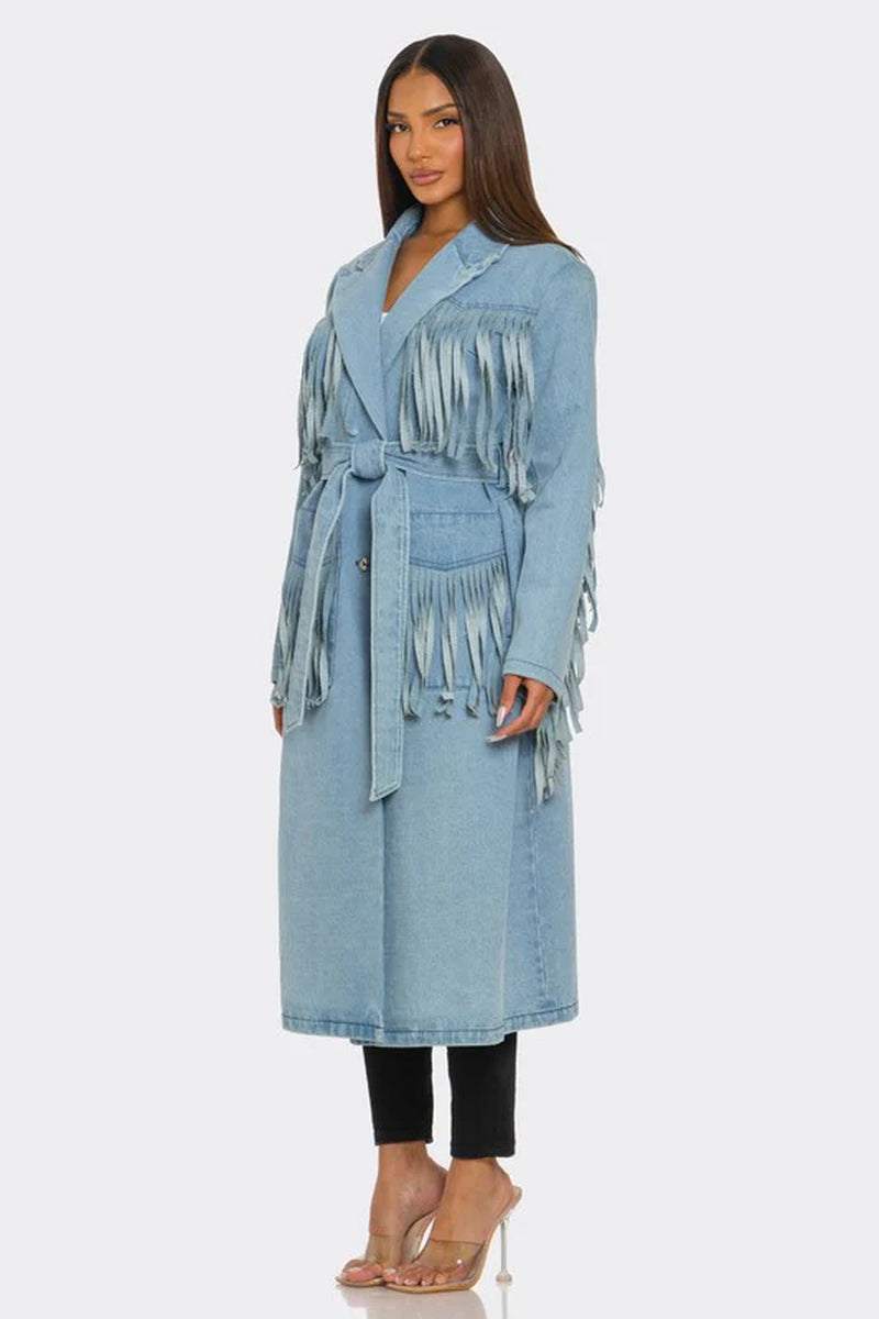Fringed longline denim trench coat with waist-cinching belt and layered detailing, styled with heeled boots.