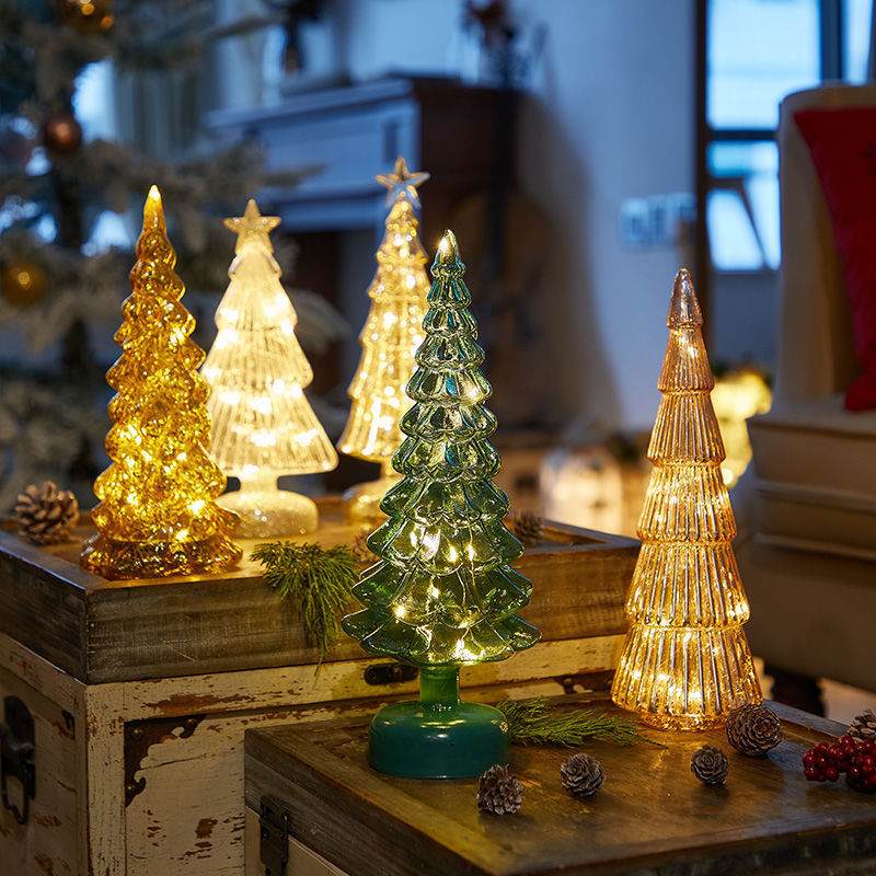 Various lit glass Christmas trees on a table, ideal for Christmas table decorations.
