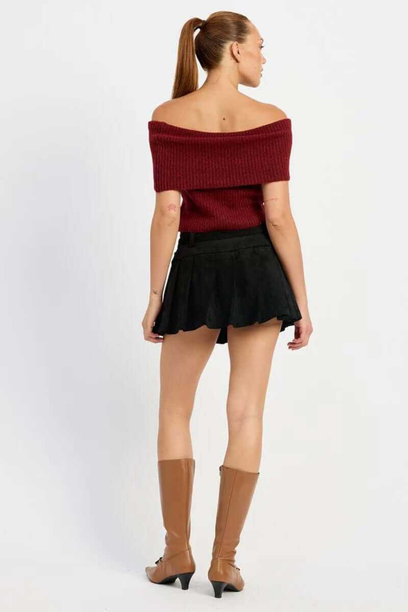 Back view of model wearing a high-waisted pleated suede belted skort with a red off-shoulder sweater and knee-high boots.