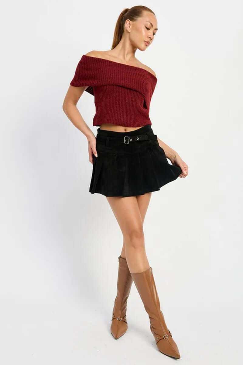 Model wearing a high-waisted pleated suede belted skort with an off-shoulder top and stylish knee-high boots.