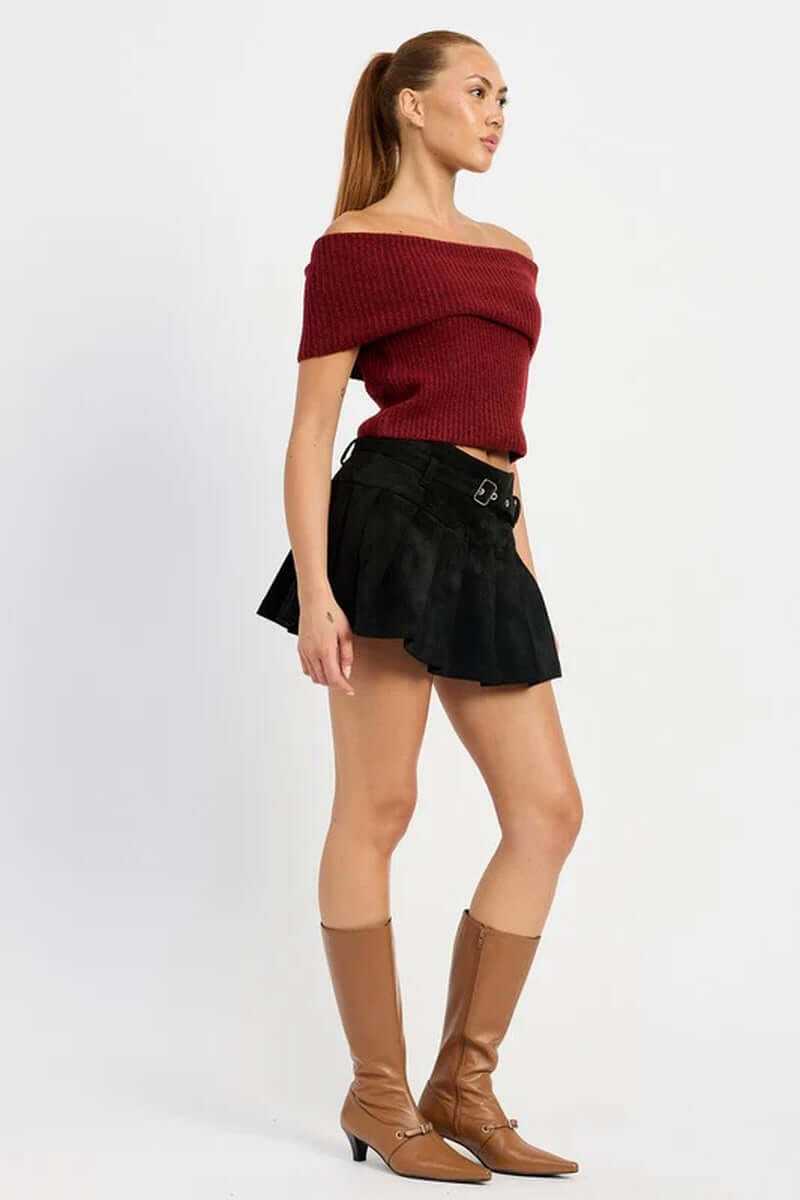 Model wearing a high-waisted pleated suede belted skort with an off-the-shoulder top and knee-high boots.