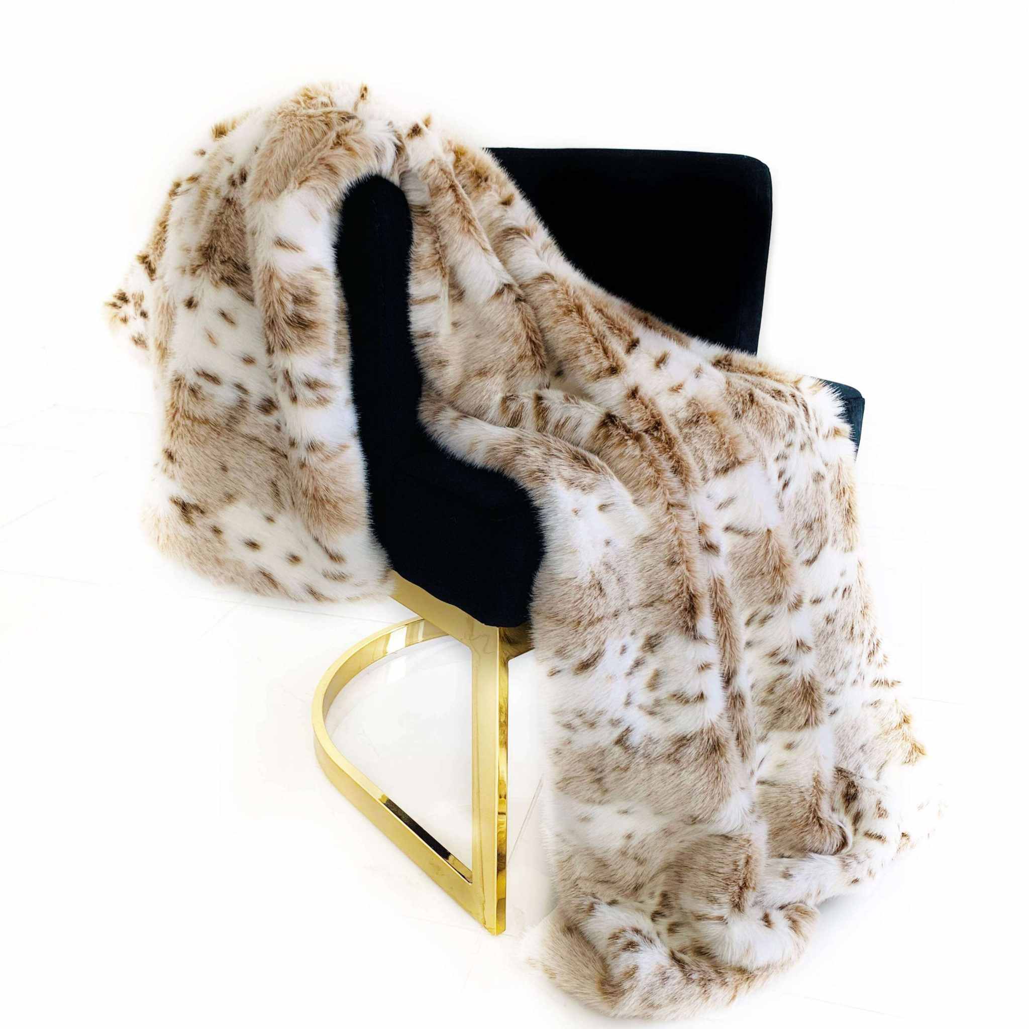 Luxury leopard faux fur throw blanket draped over a modern black chair with gold accents.
