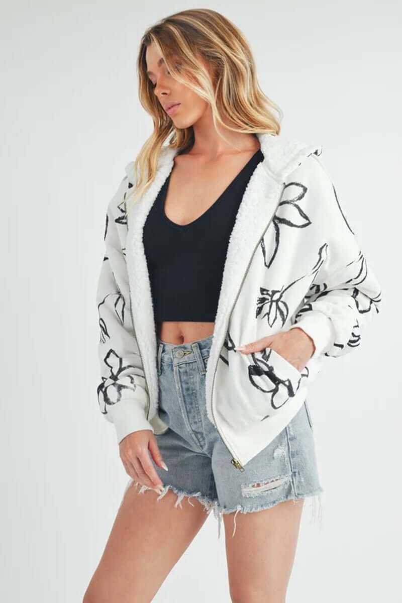 Model wearing Oita jacket with floral print, sherpa lining, oversized fit, and hand pockets, paired with denim shorts.