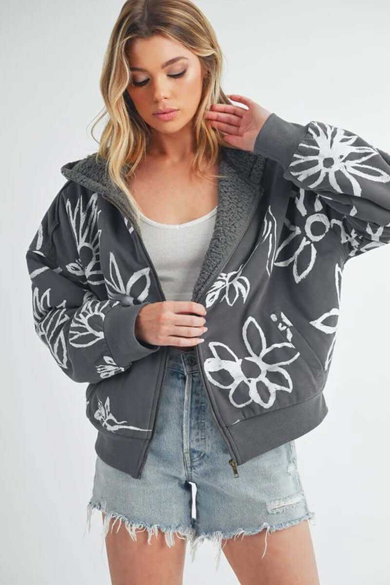 Woman wearing the Oita jacket, a cozy bomber jacket with floral print and sherpa lining, paired with denim shorts.