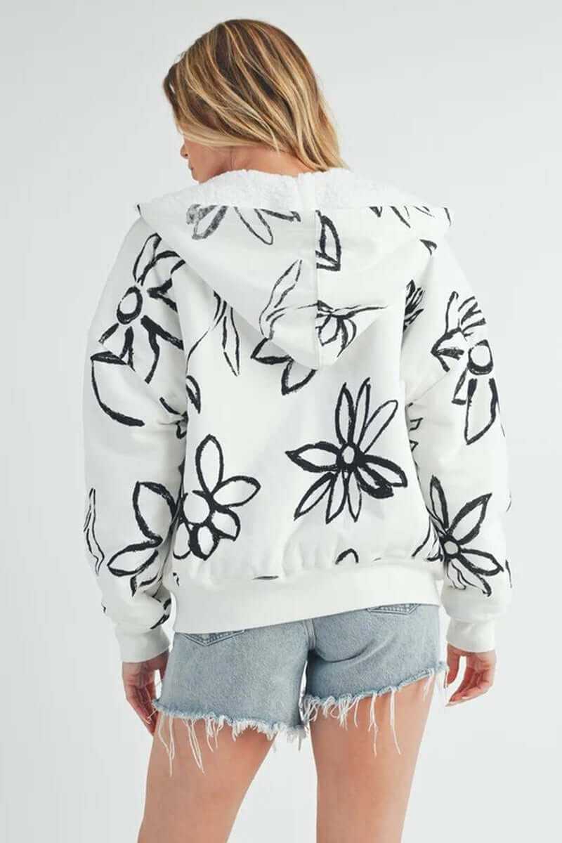 Back view of the Oita jacket with floral print, hood, and ribbed cuffs, paired with denim shorts.