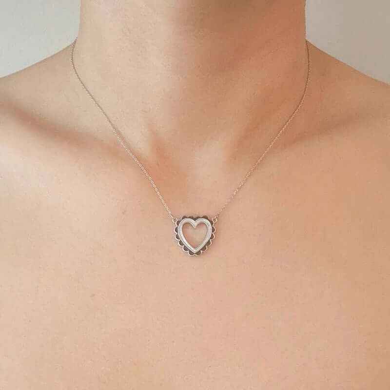 Scallop edged heart necklace worn on a bare neck showcasing elegant design in silver.