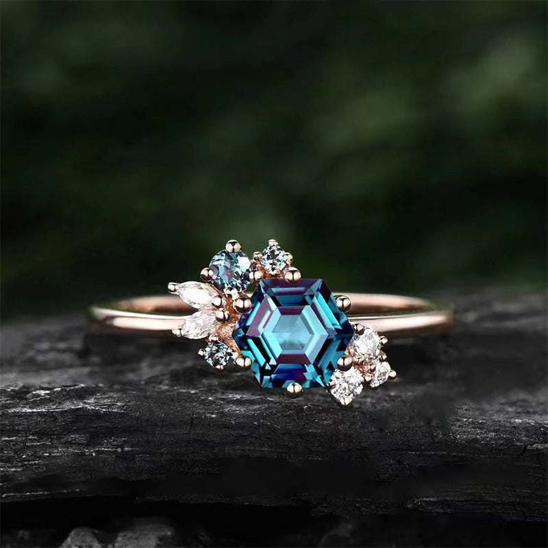 Prismatic Brilliance Six-Claw Zircon Ring with blue geometric center stone and small clear zircon accents in rose gold setting