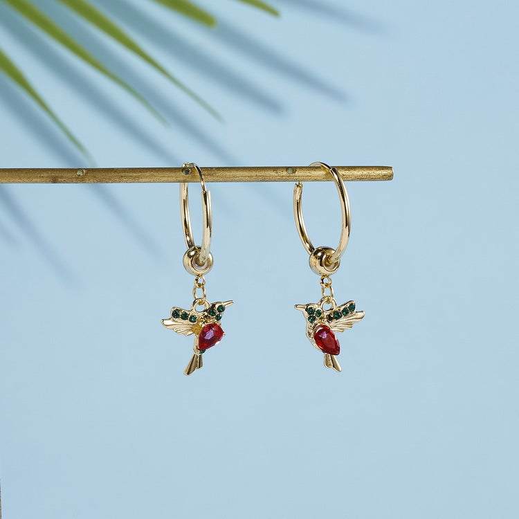 Gold hoop earrings with red and blue hummingbird charms on light blue background