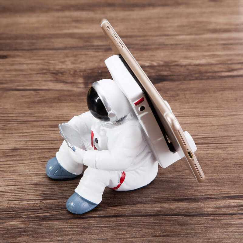 Cute astronaut mobile phone stand in white resin holding a smartphone, perfect for desk decoration and as a creative gift.