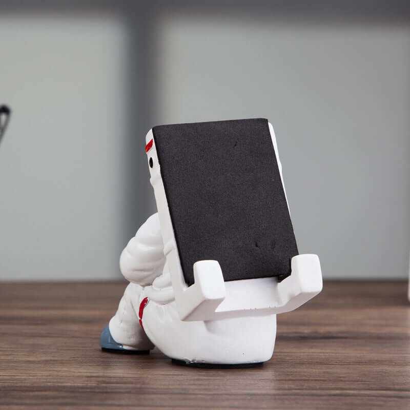 Cute astronaut mobile phone stand with black backing, perfect for desks and creative gifts.