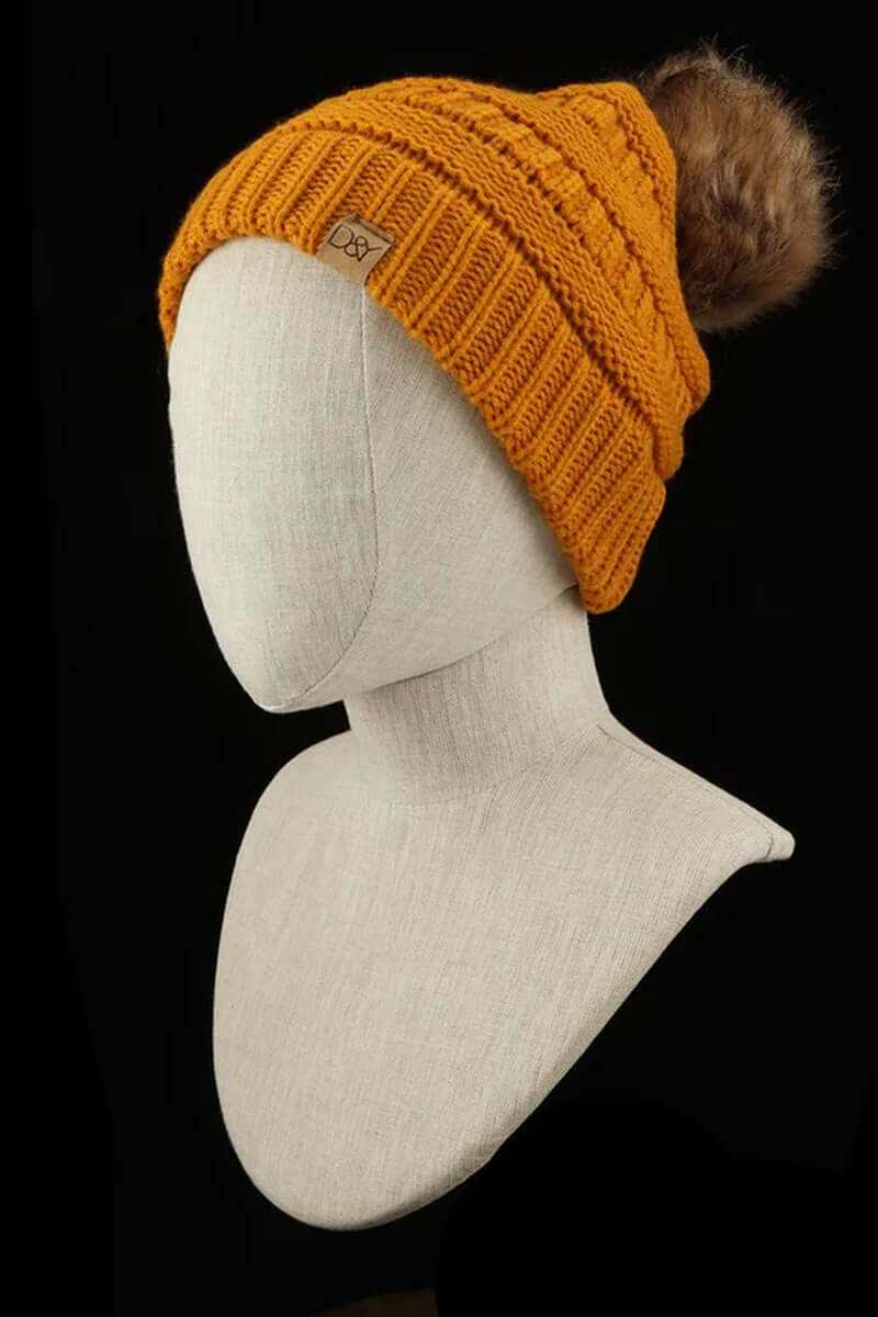 Super soft halo ripped faux fur pom beanie in mustard yellow on a mannequin, perfect for trendy winter style.
