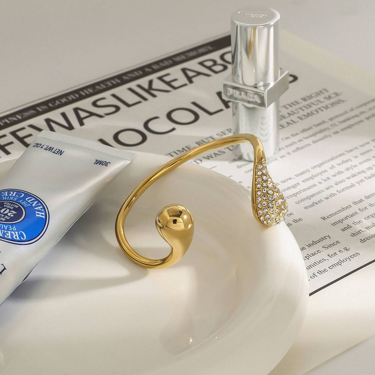 Gold titanium steel bracelet with diamond water drop design on white ceramic dish