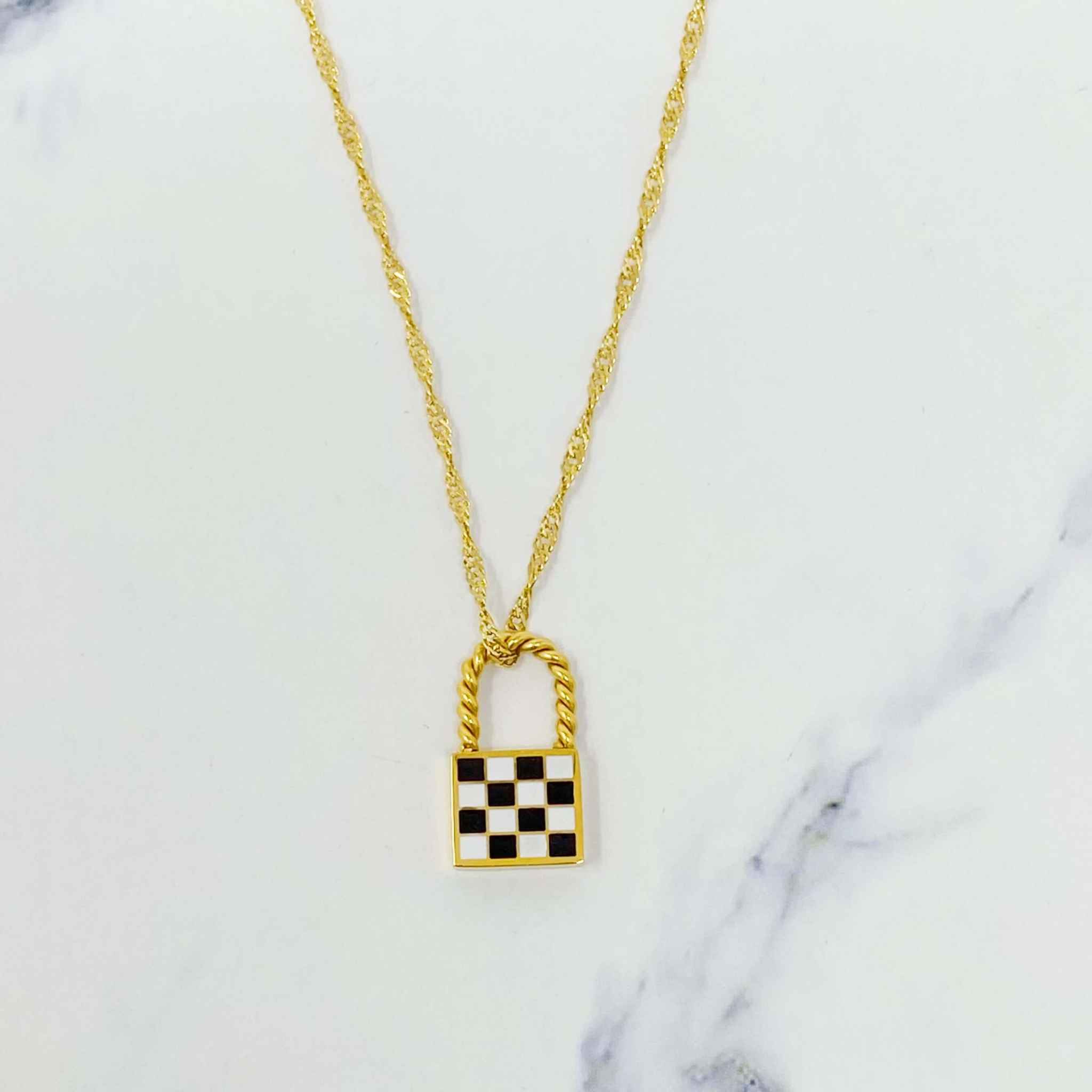 Trendy vintage checkered locket pendant necklace with a golden twist chain on marble background.