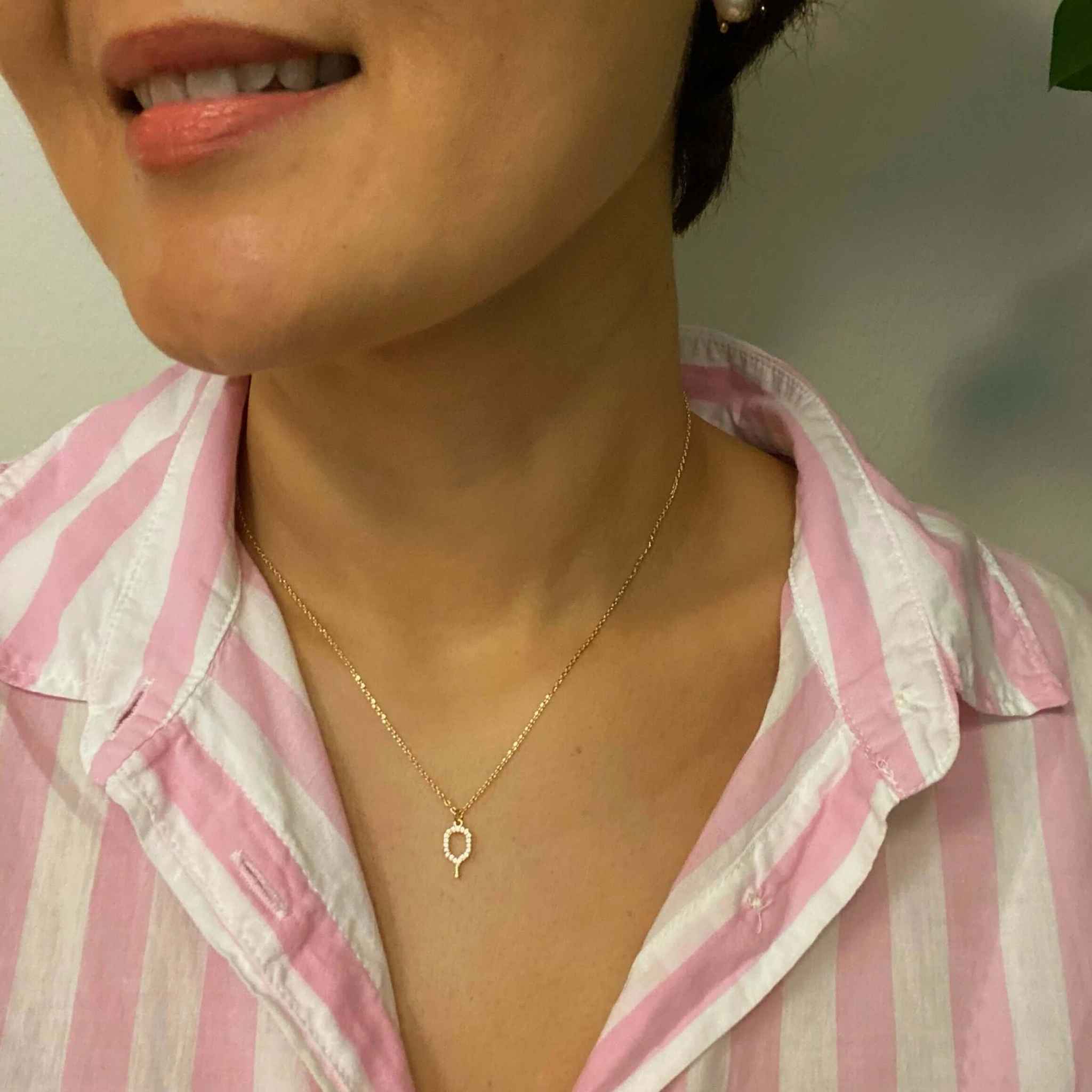 Close-up of a woman wearing a dainty gold pickleball pendant necklace with pink striped shirt.