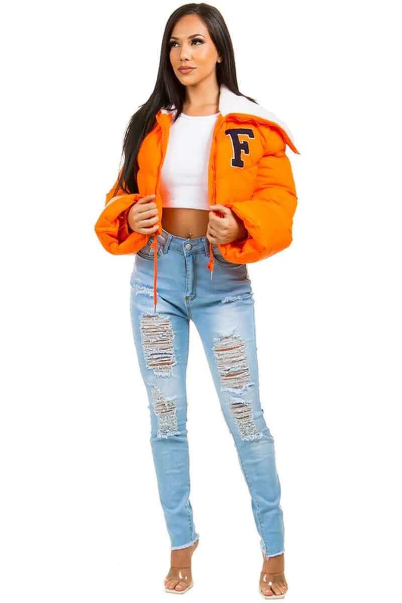 Model wearing an orange puffer jacket with a white hood and ripped blue jeans, showcasing a trendy oversized look.
